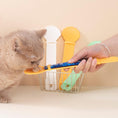 Load image into Gallery viewer, A cat being fed with a yellow cat treat spoon by a person, with two additional spoons hanging in the background.